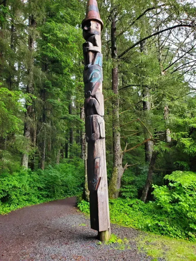 Tlingit Wolf Pole at Sitka National Historical Park, Alaska, carved figure of a wolf flanked by a fish and a human in a tall hat